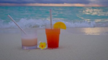Gün batımında kokteylleri yakın. İki içki standı. Arka planda mavi turkuaz okyanus. Yaz tatili konsepti. 4k ağır çekim videosu. 