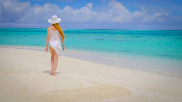 ビキニ姿の女が白い帽子をかぶって歩いている 女性はモルディブで幸せである 背景に青いターコイズブルーの海 女の子は熱帯の休日を楽しんでいます 夏の旅行休暇のコンセプト — ストック写真