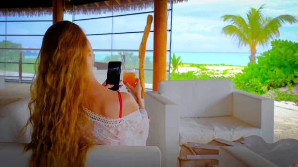 핸드폰을 칵테일을 마시는 몰디브의 잔하는 청록색 배경에 있습니다 소녀는 휴일을 — 스톡 사진