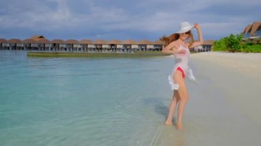 Bikinili kadın dönüyor. Kadın Maldivler 'de mutlu. Arka planda mavi turkuaz okyanus. Kız tropikal tatillerin tadını çıkarıyor. Yaz tatili konsepti. Yavaş çekim 4k video.
