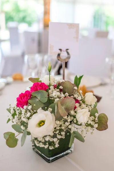 Wedding reception photo. Glasses and flowers on tables. Empty wedding label. Name tag. Wedding restaurant white interior decor, no people.