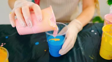 Fluid art technique. Female artist works on abstract fluid art painting, mixing acrylic colors. Painter in process create artwork in an art studio. 