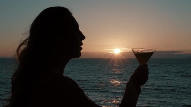 日落时一个女人在海滨端着鸡尾酒的轮廓 背景是太阳和大海 暑假的气氛 全高清录像 — 图库视频影像
