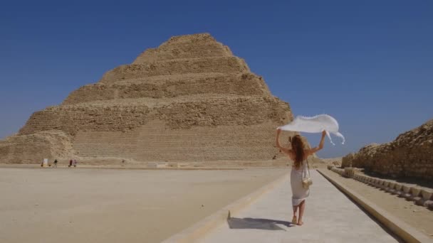 穿着白色衣服的女人走着 手里拿着一块白色的面料 背景是Djoser Step 考古遗存于埃及 非洲的萨卡拉墓地 旅行旅游概念 — 图库视频影像
