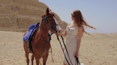Beyaz elbiseli kadın ayakta ve bir atla gülümsüyor. Arka planda Djoser Step var. Arkeolojik olarak Saqqara mezarlığı, Mısır, Afrika. Seyahat konsepti.