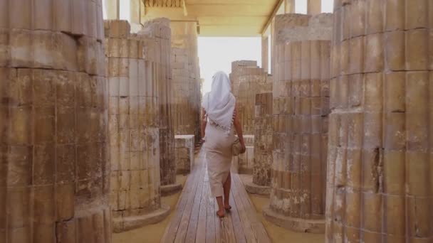 在埃及萨卡拉的Djosers阶梯金字塔建筑群中 妇女走在世界上最古老的石柱中间 女孩穿着一件白色的奇装异服和一件衣服 旅游概念 慢动作视频 — 图库视频影像