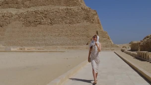 穿着白衣的女人在走路 背景是Djoser Step 考古遗存于埃及 非洲的萨卡拉墓地 旅行旅游概念 — 图库视频影像