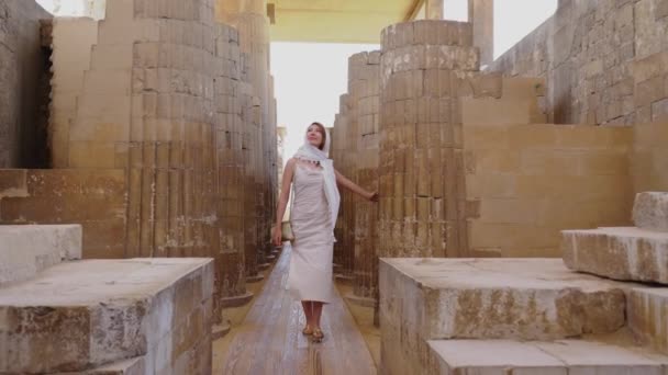 在埃及萨卡拉的Djosers阶梯金字塔建筑群中 妇女走在世界上最古老的石柱中间 女孩穿着一件白色的奇装异服和一件衣服 旅游概念 — 图库视频影像