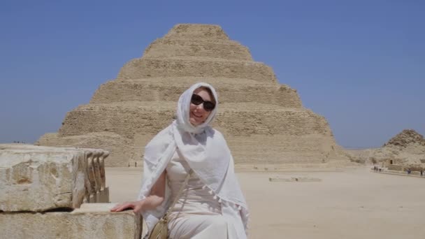 穿着白衣的女人坐在那里 背景是Djoser Step 考古遗存于埃及 非洲的萨卡拉墓地 旅行旅游概念 — 图库视频影像