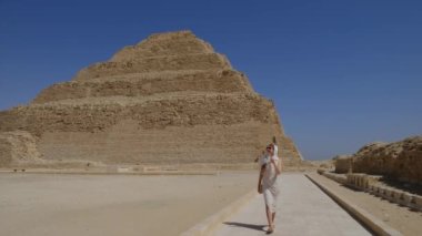 Beyaz elbiseli kadın yürüyor. Arka planda Djoser Step var. Arkeolojik olarak Saqqara mezarlığı, Mısır, Afrika. Seyahat konsepti.