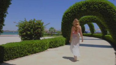 Yeşil kavisli bir yolda yürüyen bir kadın. Güzel, uzun saçlı bir kız. Yavaş çekim videosu. Arka planda deniz ve palmiyeler. 