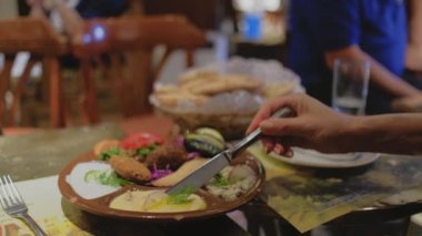 Mısır yemeği masanın üzerindedir. Bıçaklı bir kadın eli tandır roti ekmeğine sos koyuyor. Restoranda. Arap mutfağı.
