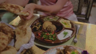 Mısır yemeği masanın üzerindedir. Bıçaklı bir kadın eli tandır roti ekmeğine sos koyuyor. Restoranda. Arap mutfağı.