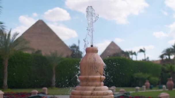 噴水の近くに ギザのピラミッドは背景にあります グレートピラミッドを望むパーム付きのラグジュアリーホテルテラス — ストック動画