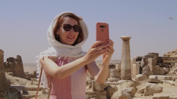 ドレスを着た女性がエジプトで自分撮りをしています ギザの大ピラミッドと背景に遺跡 オールドストーンと砂 — ストック動画
