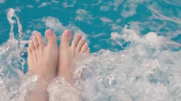 女性の足の近くに 爪にピンクの釘が磨かれ プールのターコイズブルーウォーターに水を飛ばします 水の中のバブルとバブル ジャグジー マッサージ — ストック動画