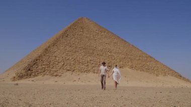 Beyaz elbiseli kadın yürüyor. Kız bir erkekle el ele tutuşuyor. Arka planda Djoser Step var. Arkeolojik olarak Saqqara mezarlığı, Mısır, Afrika. Seyahat konsepti.