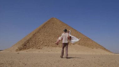 Beyaz elbiseli kadın. Adam elinde bir kadın tutuyor. Arka planda Djoser Step var. Arkeolojik olarak Saqqara mezarlığı, Mısır, Afrika. Seyahat konsepti.