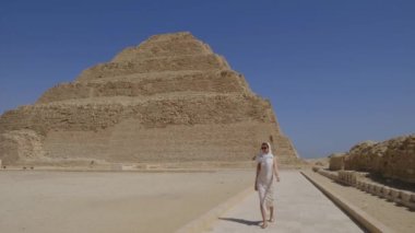 Beyaz elbiseli kadın yürüyor. Arka planda Djoser Step var. Arkeolojik olarak Saqqara mezarlığı, Mısır, Afrika. Seyahat konsepti.