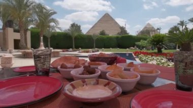 Mısır yemeği masanın üzerindedir. Restoranda. Arap mutfağı. Arka planda Giza Piramitleri var. Palmiyeli lüks otel terası ve Büyük Piramitlerin manzarası. Kadın fotoğraf çekiyor..