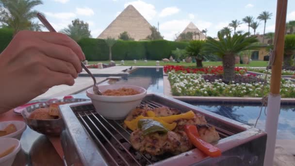 埃及菜在桌子上 女手拿着叉子捡米 阿拉伯菜 吉萨金字塔在背景上 富丽堂皇的带棕榈的酒店平台和壮观的金字塔 — 图库视频影像