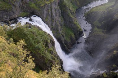 Güçlü bir şelalenin, yemyeşil ve engebeli uçurumlarla çevrili derin bir vadiye düşüşünün nefes kesici bir görüntüsü. Sis, dramatik bir şekilde havaya yükseliyor. Yüksek kalite fotoğraf.