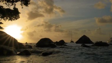 Seyşeller 'deki okyanusta altın bir günbatımını yakalıyor. Dalgalar kayalara ve yelkenlilere çarpıyor. Yavaşça uzaklarda süzülüyor..