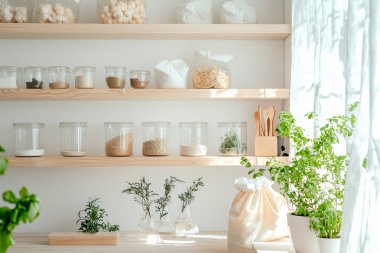 Cam kavanozlar, bambu kaplar, yeniden kullanılabilir pamuk torbaları, ahşap raflar ve saksı bitkileri gibi çevre dostu aksesuarların yer aldığı şık bir sıfır atık mutfağı.. 