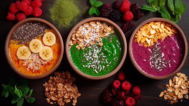 Berry, Granola ve Fresh Fruit ile canlı meyve suyu kaseleri. Chia, granola, taze böğürtlen ve hindistan cevizi gibi süper yiyeceklerden yapılmış sağlıklı meyve sulama kaseleri koyu ahşap arka planda renkli ve parlak bir kompozisyonda dizilmiştir.. 
