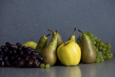 Gri arka planda armutlar, elmalar ve üzümlerle dolu sonbahar meyveleri.