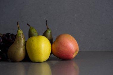 Gri arka planda armutlar, elmalar ve üzümlerle dolu sonbahar meyveleri.