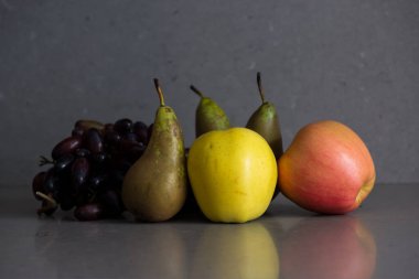 Gri arka planda armutlar, elmalar ve üzümlerle dolu sonbahar meyveleri.