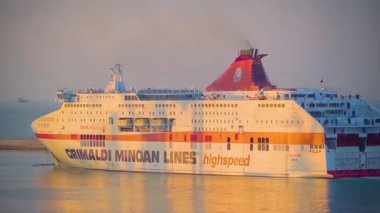 Gün batımında büyük bir feribot, çarpıcı renkleri sudan yansıyarak limana yaklaşır. Bu sahne, gemi yanaşmaya hazırlanırken sakin atmosferi yakalar. 