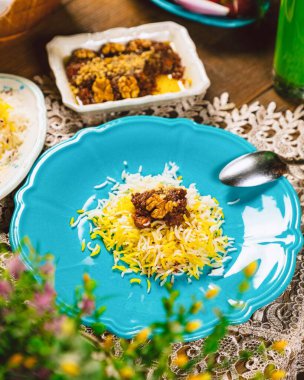 Saffron basmati rice with fesenjan stew made of chicken, walnuts and pomegranate molasses, served on a blue plate on a decorated table clipart