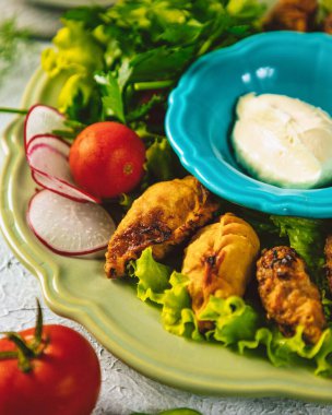 Kızarmış gyoza köfteleri, yanında sos ve taze sebzelerle yeşil bir tabakta servis edilir.