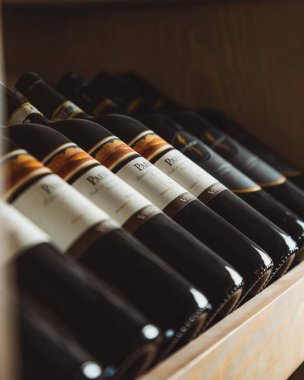 Ahşap bir rafta duran şarap şişeleri etiketlerini sergiliyor.