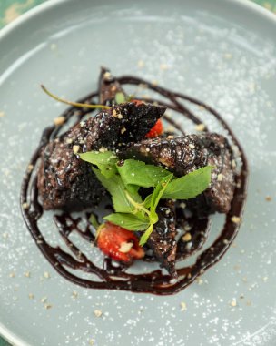 Çikolatalı browni dilimleri üzerine çikolata sosu, çilek, nane ve ezilmiş fındık.