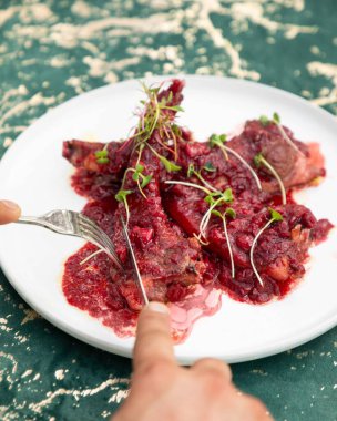 Kızılcık soslu ızgara kuzu kaburgası ve mikro yeşiller beyaz tabakta bir şef tarafından kesiliyor.