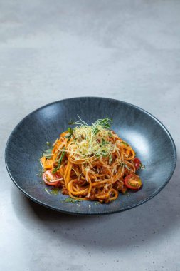 Bir tabak spagetti bolonez peynirli ve otlu, modern mavi bir tabakta duruyor.