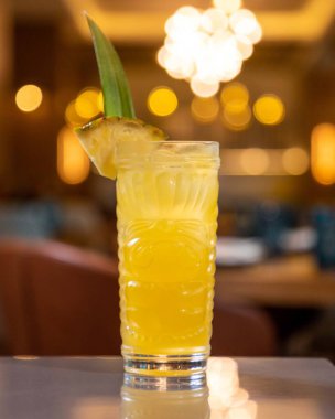 Tiki tarzı bardakta servis edilen ananas kokteyli barın üzerinde bulanık restoranın arka planında duruyor.
