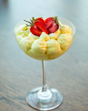 Lezzetli kremalı tatlı ve taze çilek ahşap bir masada zarif bir bardakta servis edilir.