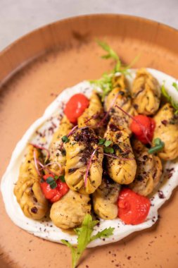 Beyaz soslu kızarmış hamur köfteleri tabakta servis ediliyor ve mikro yeşilliklerle süsleniyor.