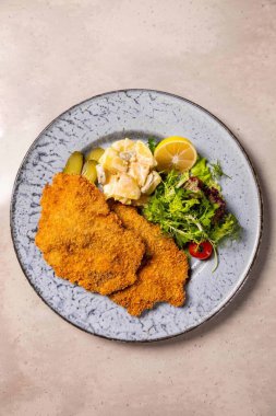 Patates salatası, turşu, limon ve taze yeşilliklerle servis edilmiş iki parça kızarmış şnitzel.