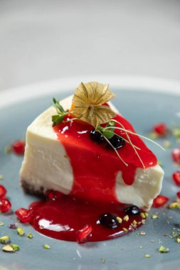 Kırmızı böğürtlen soslu kremalı cheesecake, physalis ve şam fıstığı parçacıklarıyla süslenmiş.