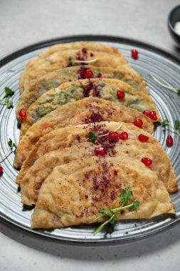 Birkaç qutab hamur işi bir tabağa konur, sumac serpiştirilir ve nar tohumları ve mikro yeşilliklerle süslenir.