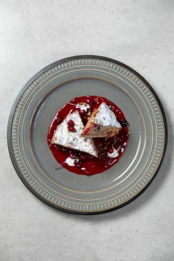 İki dilim lezzetli pasta ve çilek sosu modern bir tabakta duruyor.