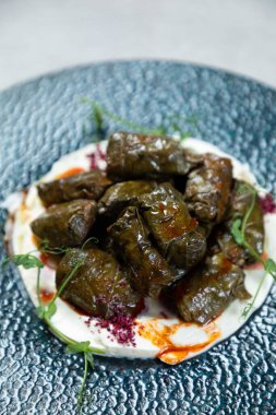 Kremalı yoğurt sosuyla servis edilen içi doldurulmuş üzüm yaprakları ve üzerine kırmızı baharatlar serpiştirilmiş.