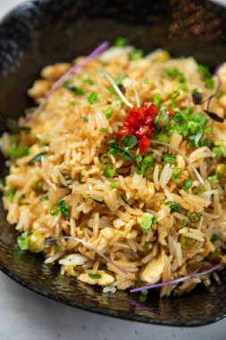 Lezzetli kızarmış pirinç bezelye, yumurta ve otlar siyah bir kasede servis edilir.