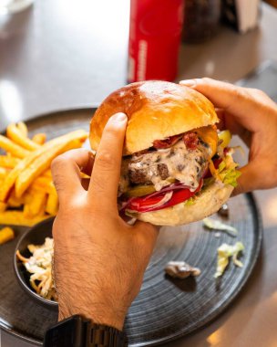 Elinde erimiş peynirli, pastırmalı ve sebzeli sulu bir hamburger tutan adam lezzetli bir yemeğin tadını çıkarıyor.