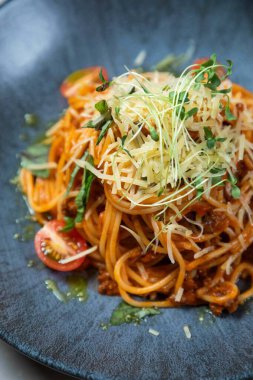 Domates soslu spagetti, taze fesleğen, parmesan peyniri ve mikroyeşillik, mavi tabakta servis edilir.
